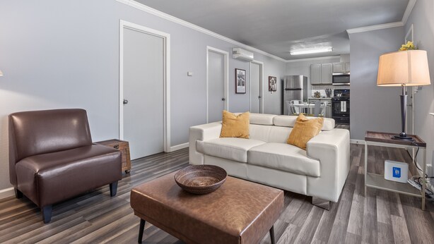 Un salon moderne avec un canapé en cuir marron, un canapé blanc agrémenté de coussins jaunes, une table basse en bois et une lampe posée sur une table d’appoint.