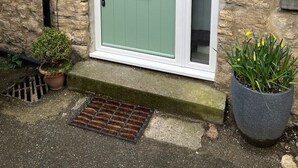 Un bâtiment en pierre avec une porte verte, une petite plante en pot et une grille d’évacuation.