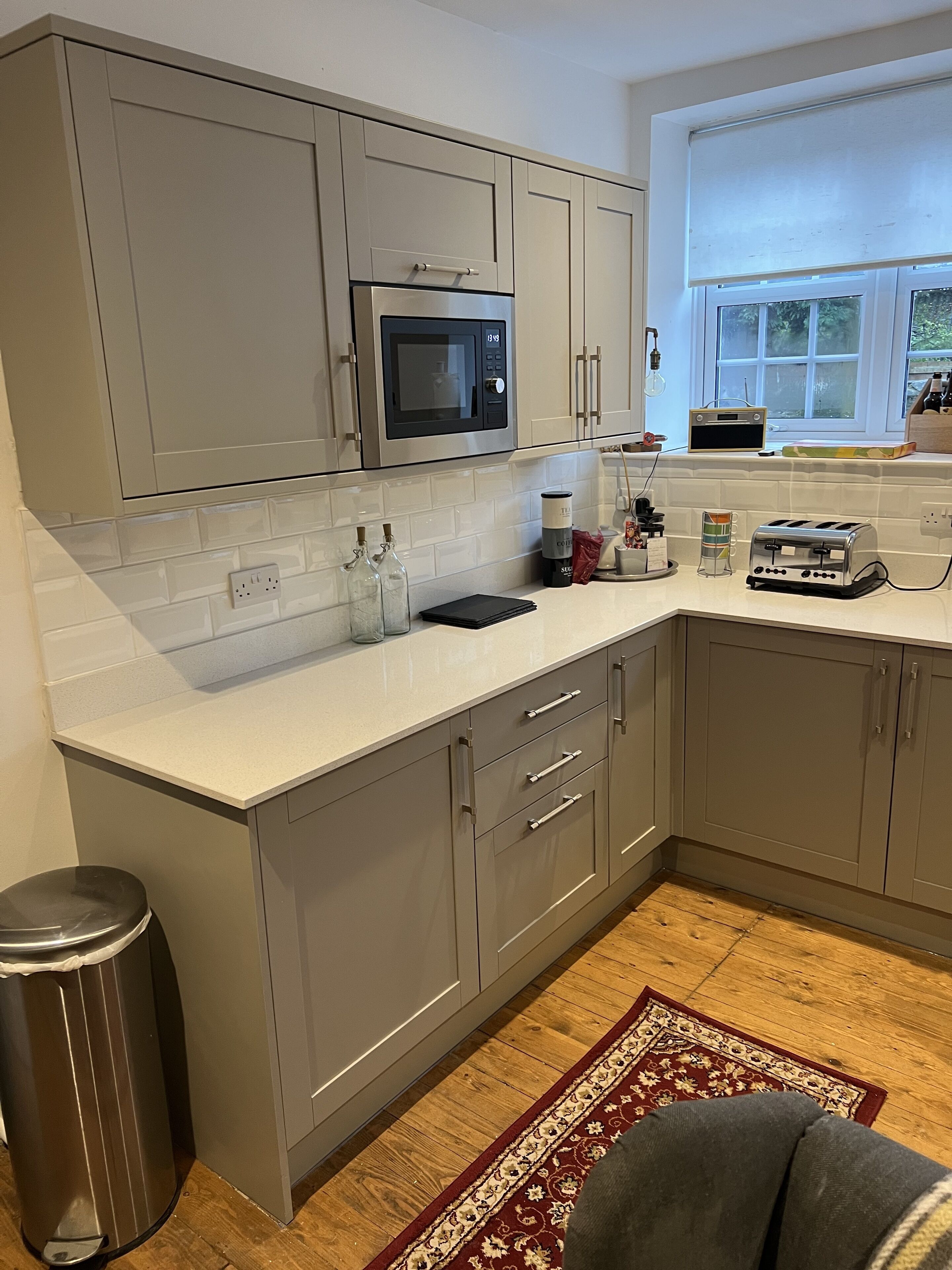 A modern kitchen with grey cabinets, a stainless steel microwave, a toaster, and a window with a view of greenery.