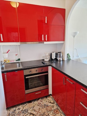 Eine Küche mit roten Schränken, einer schwarzen Arbeitsplatte, einem Edelstahlbackofen und einem Fliesenboden mit Muster.