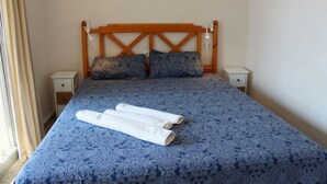 A neatly made bed with a blue patterned bedspread, two pillows, and two rolled towels on the bed. - Cozy apartment with pool (Nerja)