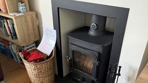 A room with a black wood-burning stove, a wicker basket with papers, and a bookshelf filled with books and magazines.