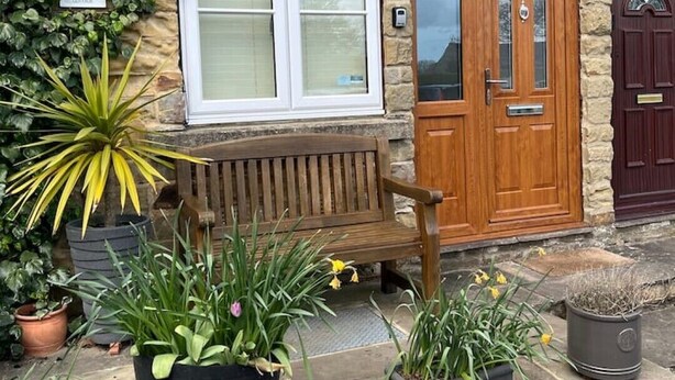 A stone building with a wooden bench, a door, and potted plants.