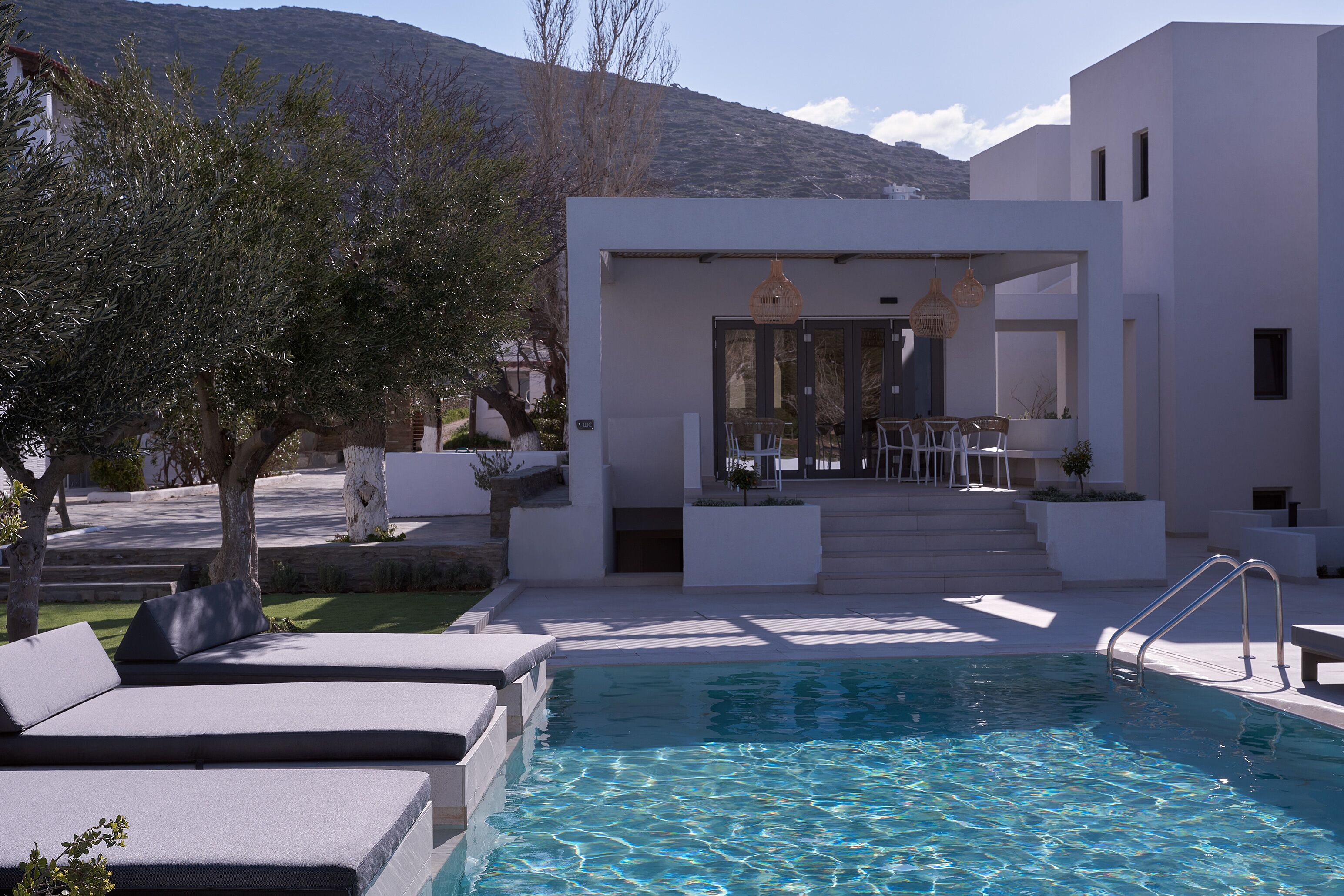 A modern pool area with a clear pool, outdoor seating, and a building with a patio.