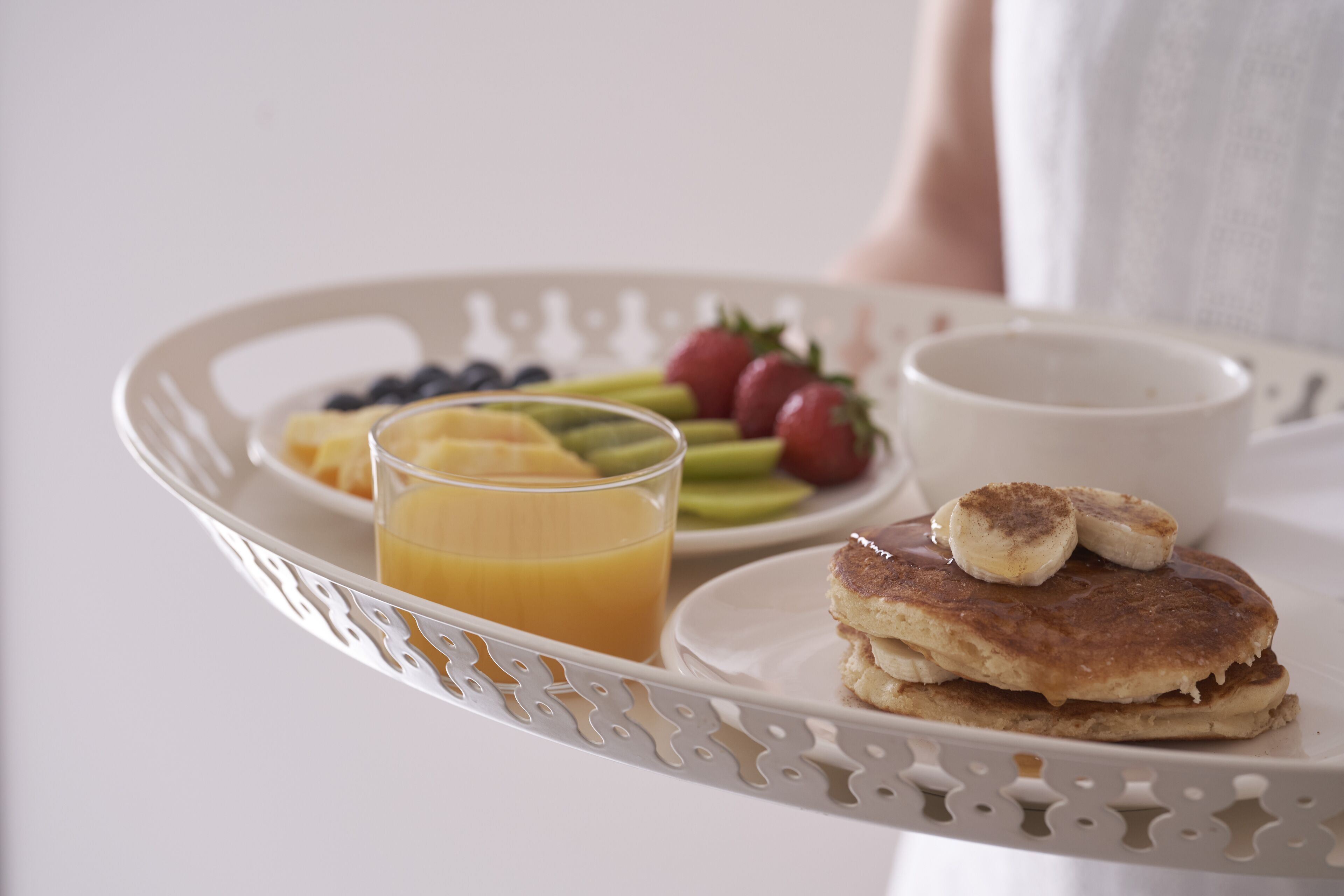 Tarjoilualusta, jossa on pannukakkuja, hedelmiä ja appelsiinimehua.