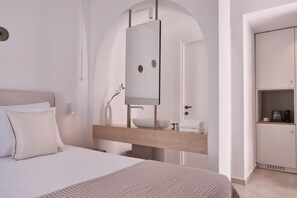 Un dormitorio moderno con una cama grande, una mesita de noche de madera, un espejo integrado y una pequeña zona de kitchenette.