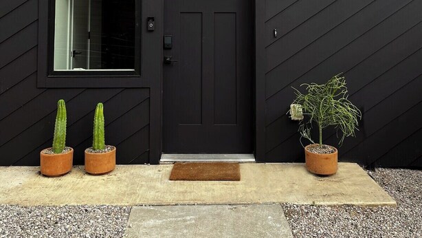 Une porte noire avec une fenêtre au-dessus, deux cactus en pot et une plante en pot sur la droite.