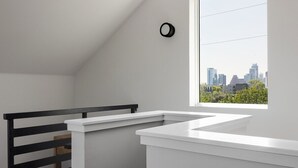 Une pièce avec un plafond blanc, une rambarde noire et une fenêtre donnant sur le panorama de la ville.