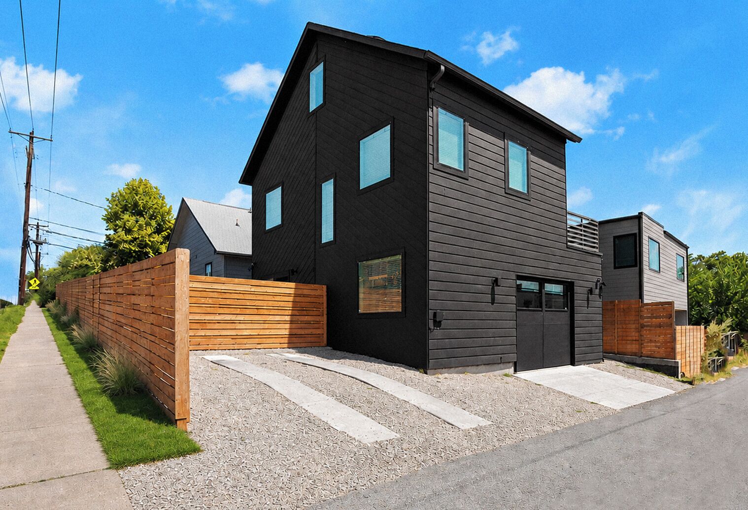 Ein modernes, zweistöckiges Haus mit dunkler Fassade, einer Garage und einem Holzzaun.