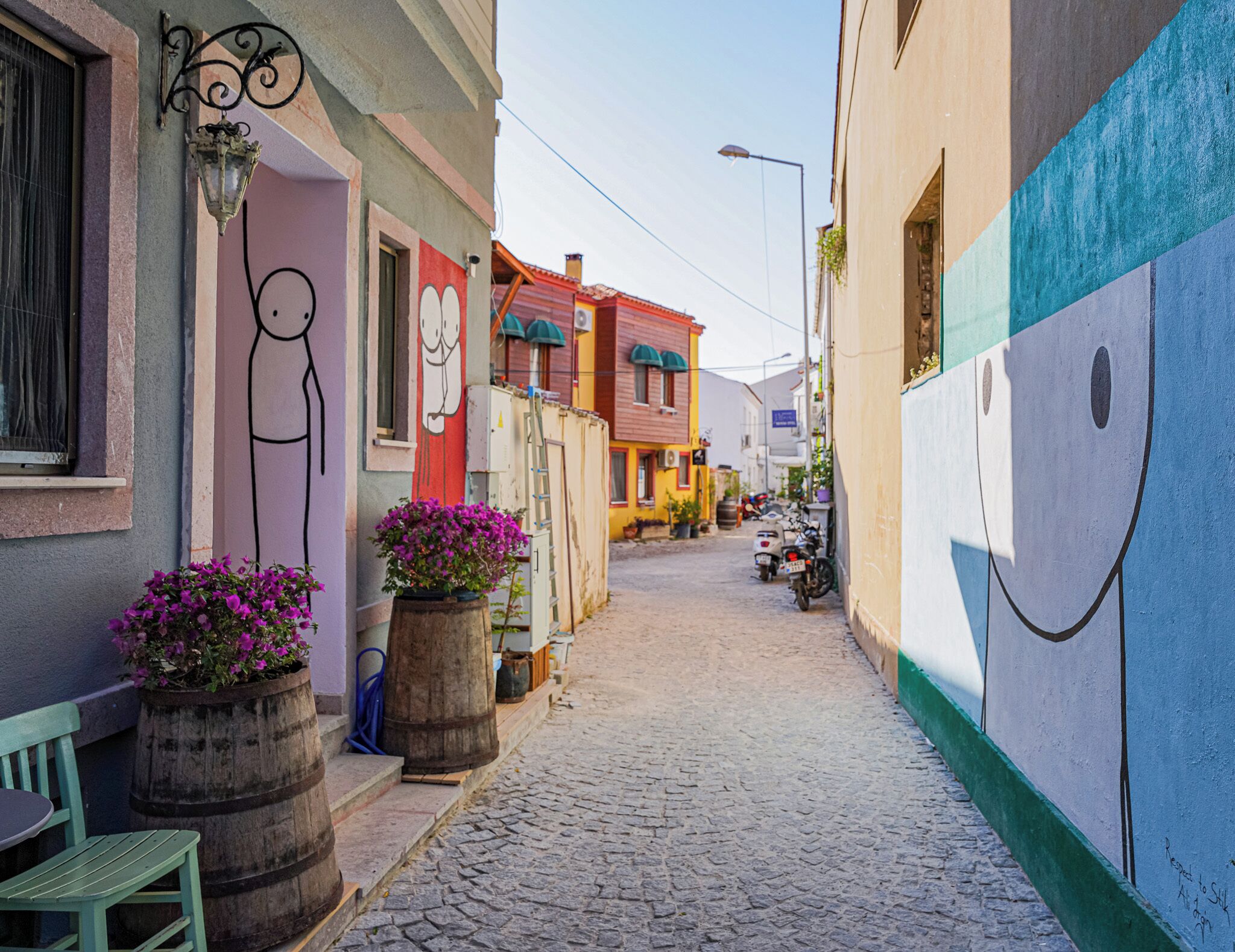 A narrow cobblestone street lined with colorful buildings, some with murals, and a few parked scooters.