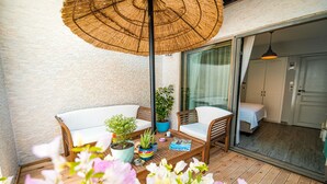 A balcony with a wooden floor, a wicker umbrella, a sofa, a chair, and a table with potted plants. - Nirvana Otel  (Bozcaada)
