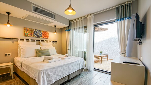 A modern hotel room with a large bed, a desk, and a view of the sea. - Nirvana Otel  (Bozcaada)