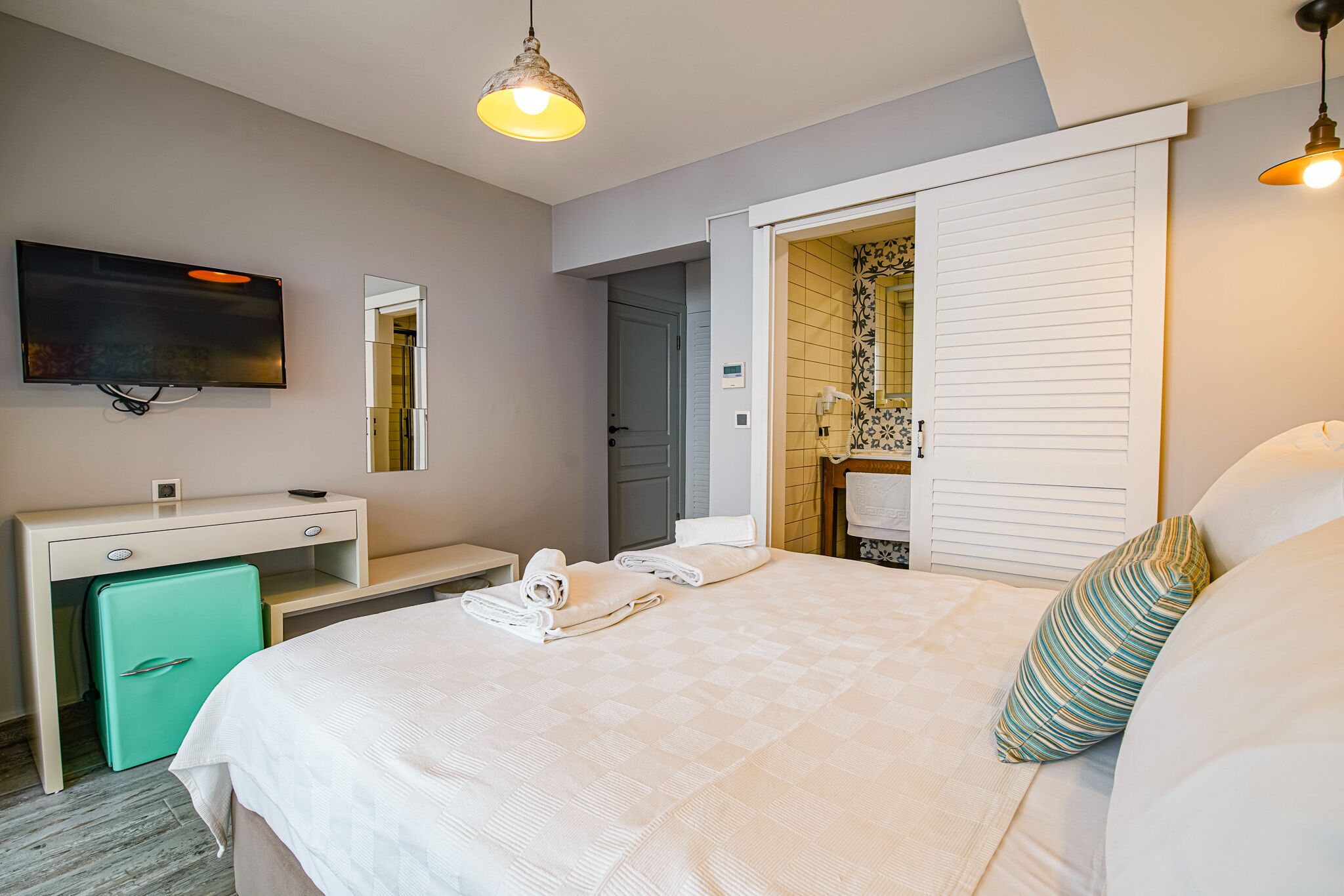 A hotel room with a bed, a desk, a television, and a bathroom visible through an open door.