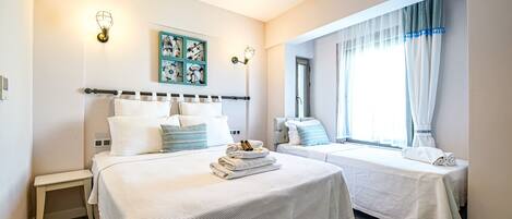 A hotel room with two beds, a bench, a wall clock, and a window with curtains.