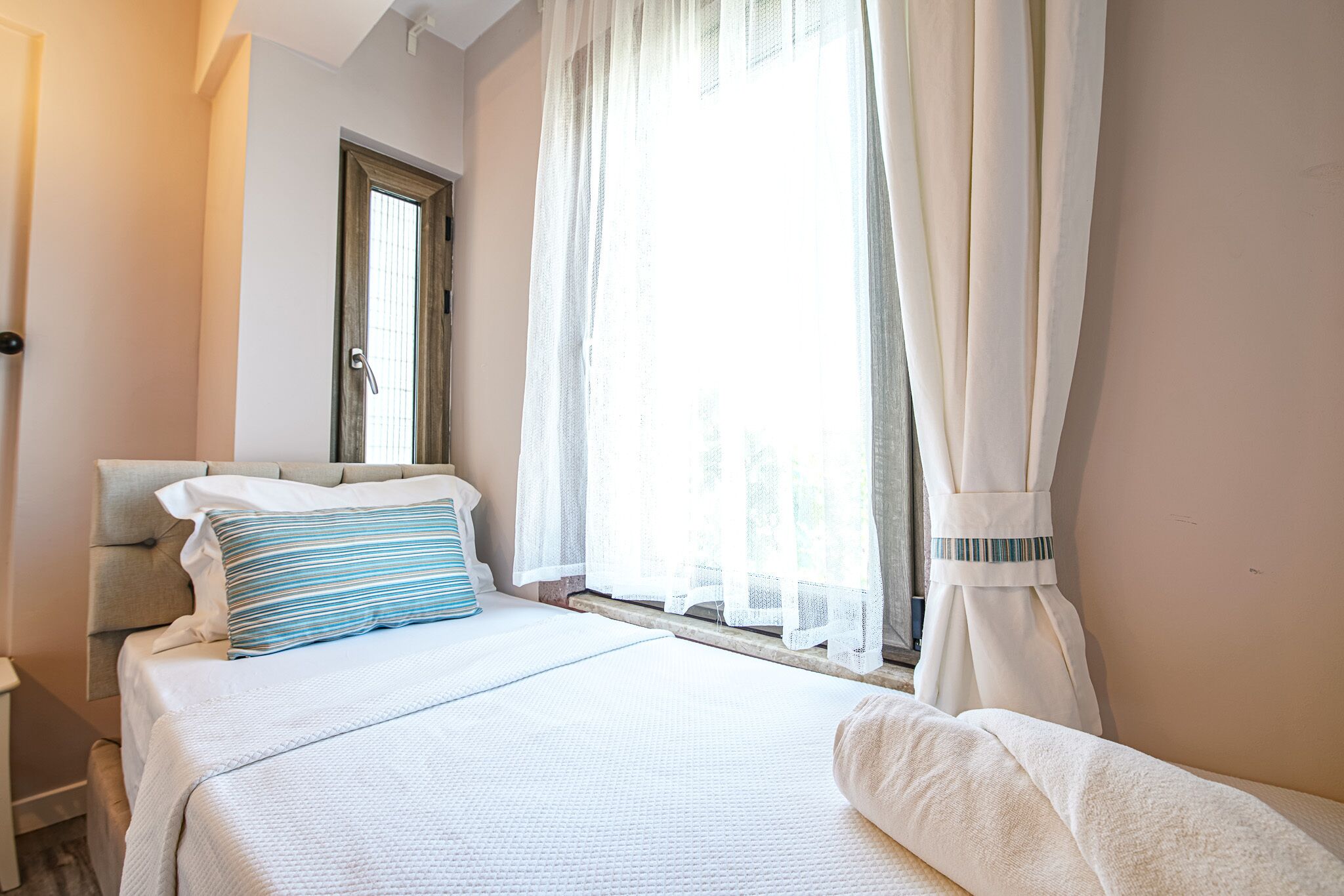 Habitació d'hotel amb un llit, una finestra amb cortines lleugeres i vista a l'exterior.