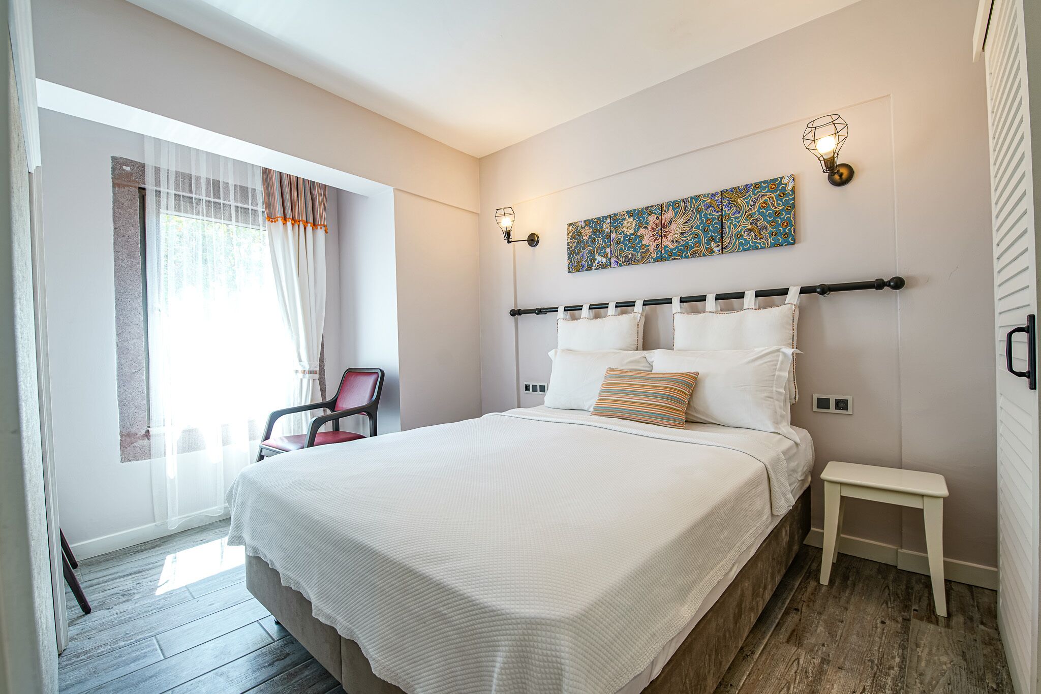 A bedroom with a large bed, a bedside table, a chair, and a window with curtains.