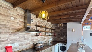 A kitchen with brick walls, wooden ceiling beams, a hanging light fixture, a built-in oven, and a washing machine. - Nirvana Otel  (Bozcaada)