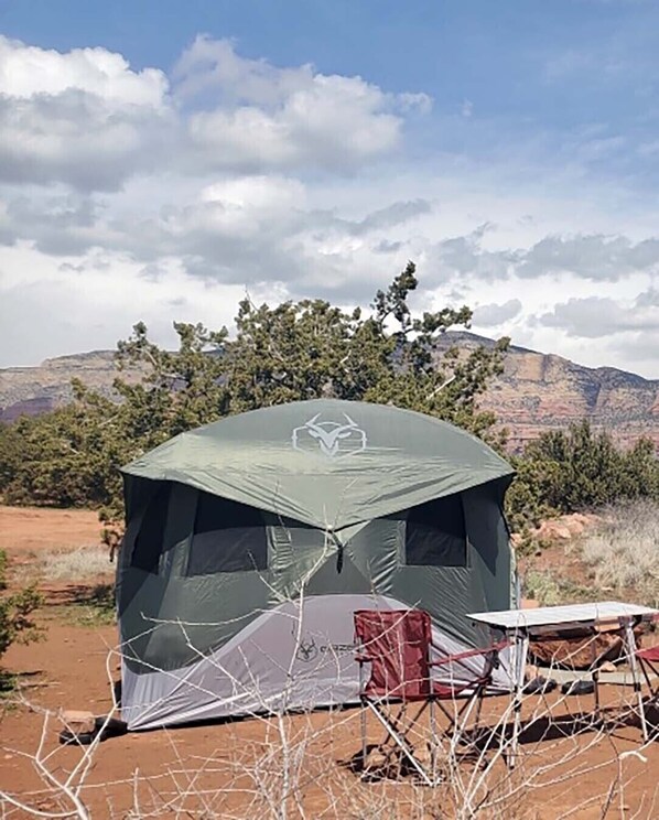 Une tente individuelle dotée d’un toit en moustiquaire, installée dans un paysage sec et dégagé, avec une végétation clairsemée et des montagnes à l’horizon.