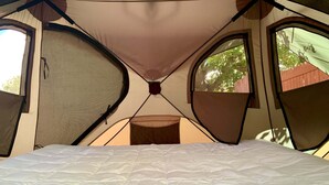 Une tente dotée d’un lit à l’intérieur, avec un poteau central et deux fenêtres.