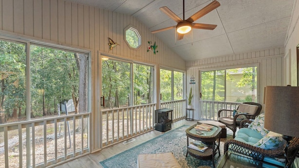 A sunroom with large windows, a ceiling fan, wicker furniture, and a fireplace.