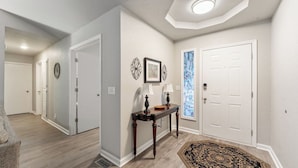 A hallway with a wooden floor, white walls, a console table with lamps, and a patterned rug.