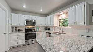 A modern kitchen with white cabinetry, stainless steel appliances, and a granite countertop.