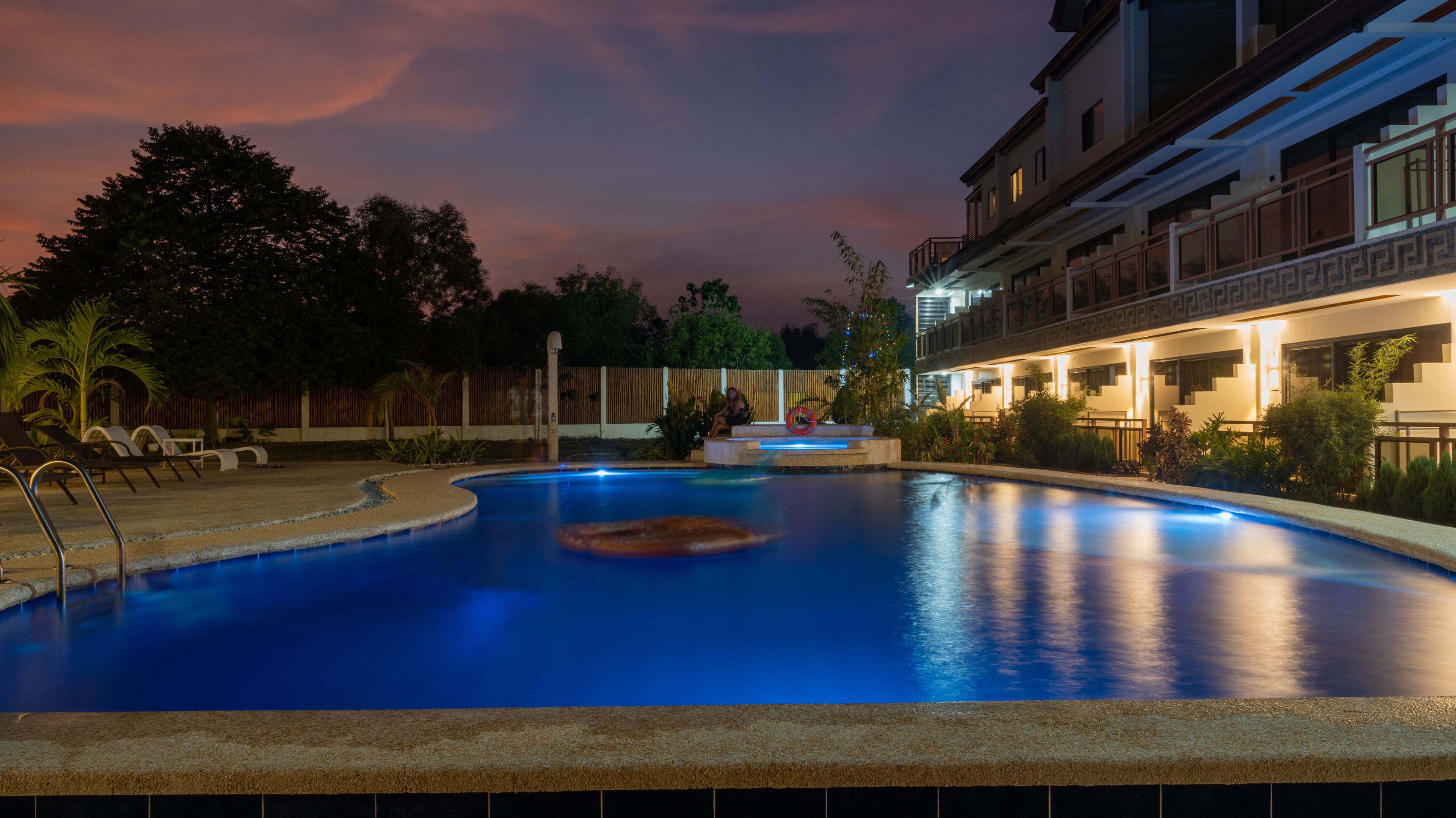 Una piscina al anochecer con vistas a un edificio con varios balcones y un paseo cubierto.