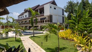 A modern two-story building with a swimming pool, surrounded by tropical plants and a stone pathway. - The Mayana Resort (Dauis)