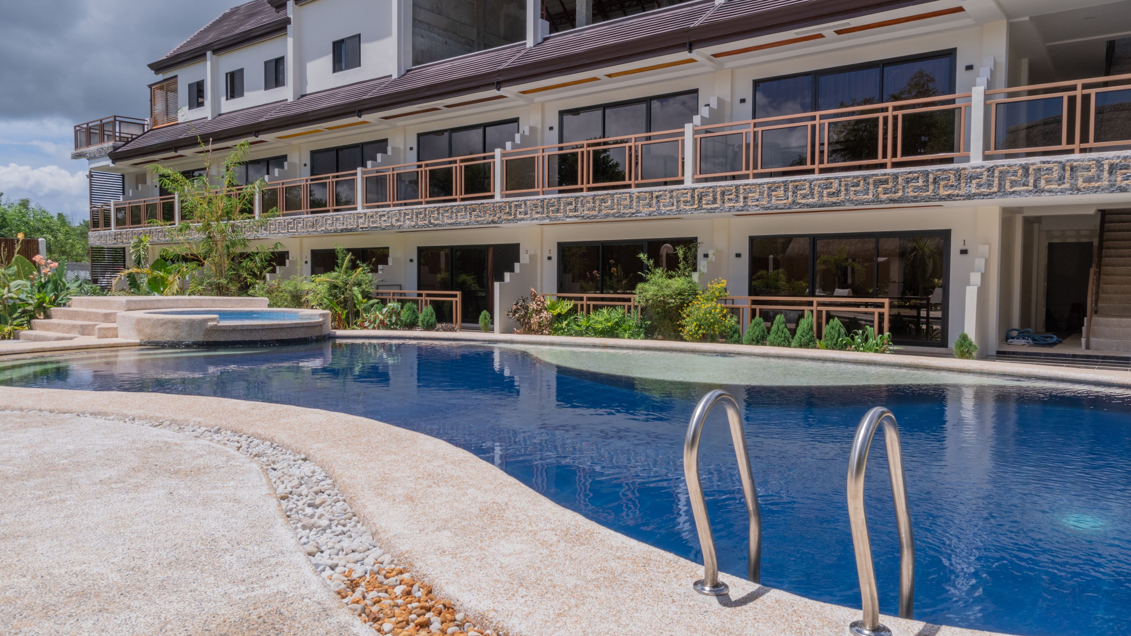 A modern hotel with a large swimming pool, outdoor seating, and a well-maintained garden.