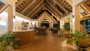 A spacious indoor area with a high ceiling and wooden beams, featuring a reception desk, seating arrangements, and potted plants. - The Mayana Resort (Dauis)