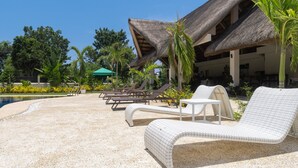 A poolside area with lounge chairs and a thatched-roof building. - The Mayana Resort (Dauis)