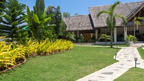 A resort with a thatched-roof building, a well-maintained lawn, and tropical plants. - The Mayana Resort (Dauis)