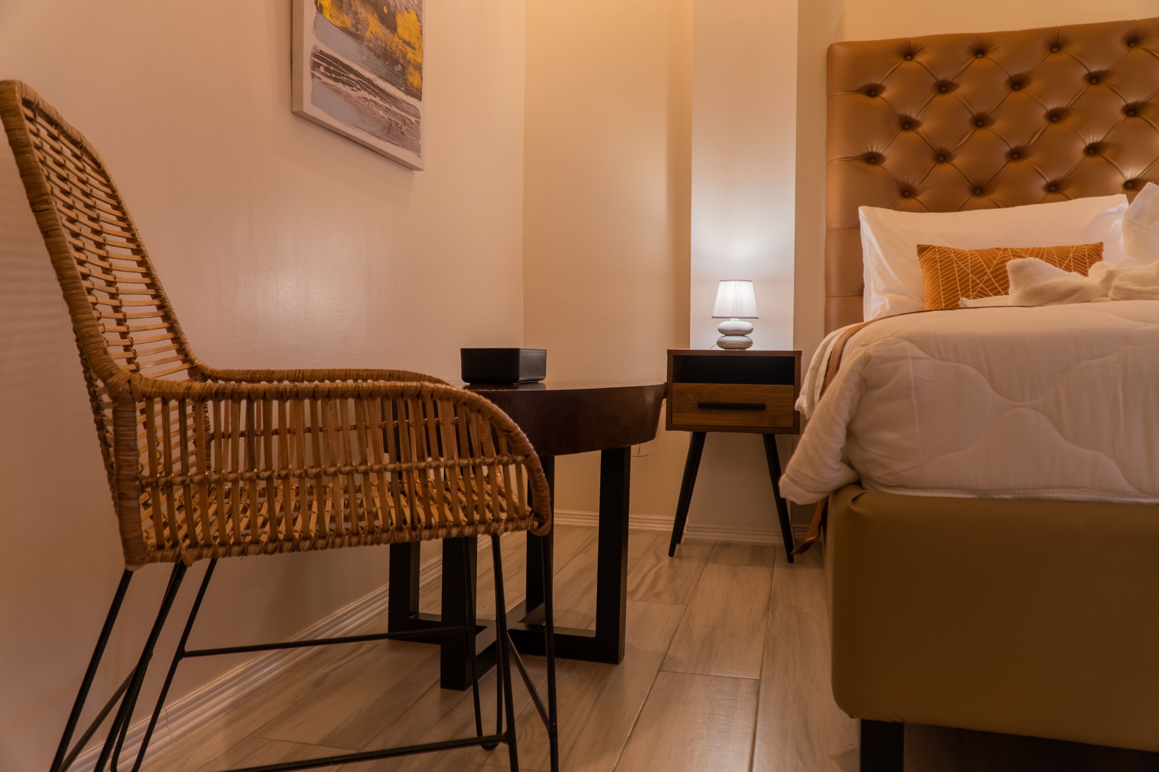 A hotel room with a bed, a chair, a small table with a lamp, and a picture on the wall.