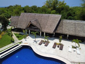 Un resort con piscina, construcciones de techo de paja y palmeras.