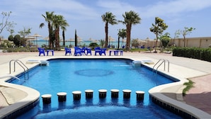 A swimming pool with blue water, surrounded by palm trees and blue chairs. - Studio flat with balcony, free access to beach and pools at Casablanca Beach (Hurghada)