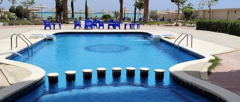 Piscina con agua azul, rodeada de palmeras y sillas azules.