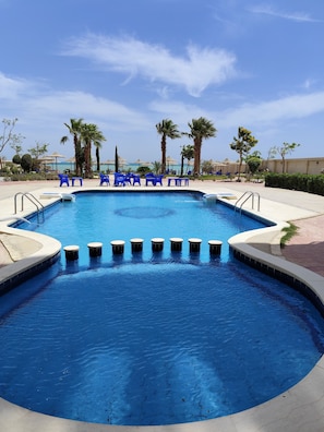 Ein Swimmingpool mit blauem Wasser, umgeben von Palmen und blauen Stühlen.