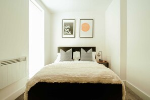 A bedroom with a bed, two pillows, a nightstand, a lamp, and two framed pictures on the wall. - Chic 2 Bedroom Apartment Salford Quays, the Lowry (Salford)