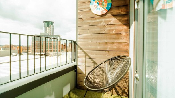 Un balcon avec une rambarde en métal, une chaise en osier et un jeu de fléchettes accroché au mur.
