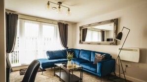 Un salon avec un canapé bleu, une table basse en verre, un lampadaire et un grand miroir au mur.