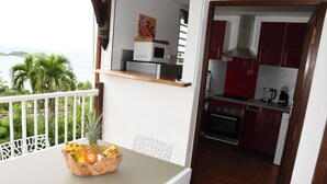 Un balcón con una mesa que sostiene un frutero, un microondas y un cuadro. Se ve la cocina, con gabinetes rojos y una estufa.
