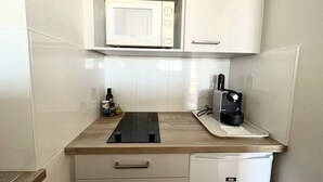 Uma cozinha compacta com micro-ondas, cafeteira e um refrigerador pequeno.