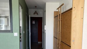 Um corredor estreito com um guarda-roupa de madeira, um pequeno banquinho e uma porta que dá para outro quarto.