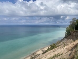Un paisaje costero con playa, aguas turquesas cristalinas y un acantilado rocoso.