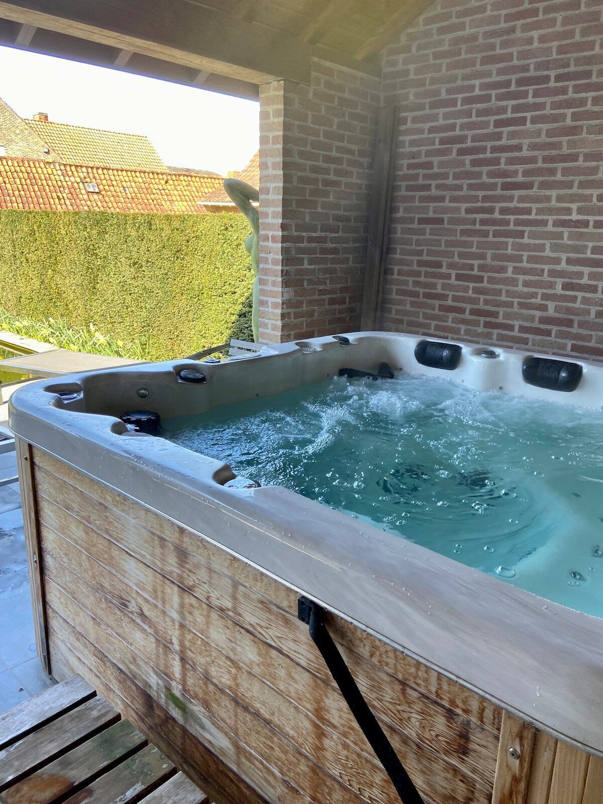 Ein Whirlpool mit Holzverkleidung, draußen gelegen mit einer Backsteinmauer und einer Hecke im Hintergrund.