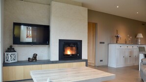 A modern living room with a fireplace, a flat-screen TV mounted above it, and a dining area with a wooden table and chairs.
