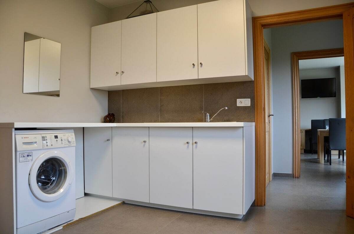Et kompakt køkken med hvide skabe, en indbygget vaskemaskine og et flisebeklædt backsplash.