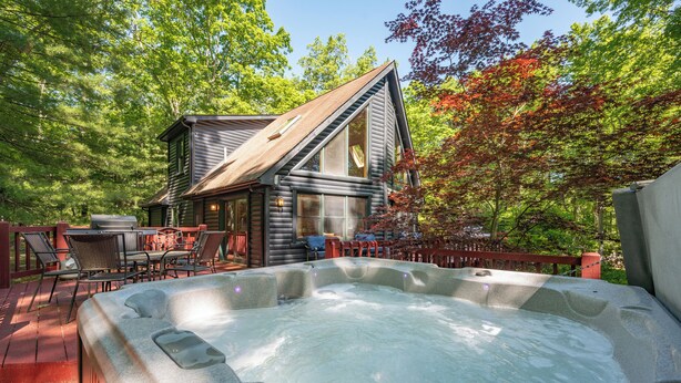 Eine Hütte mit Whirlpool, Sitzgelegenheit im Freien und einer Terrasse, umgeben von Bäumen.