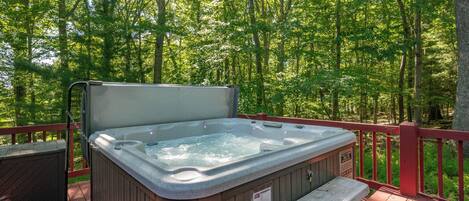 A hot tub on a wooden deck surrounded by a forest.