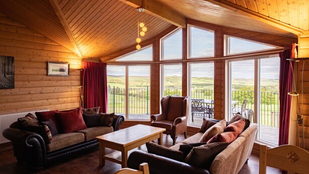 Una habitación acogedora con paredes de madera y ventanas amplias. Tiene un sofá, una silla y una mesa.